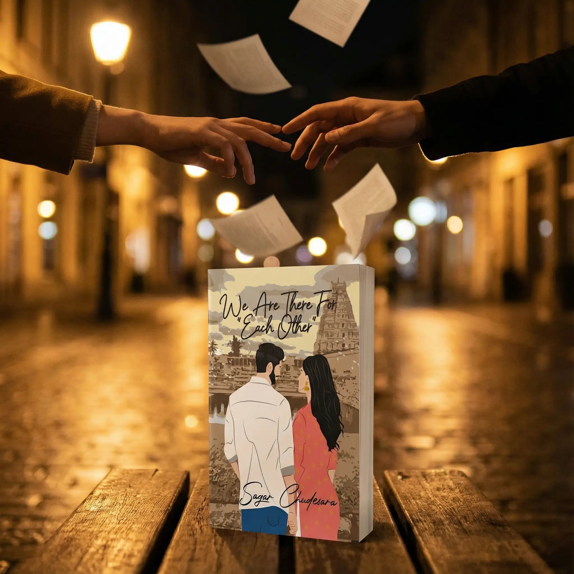 National best-seller 'We Are There For Each Other' by author Sagar Chudesara. Artistic product photography featuring flying papers and reaching hands on a romantic, lit-up city street at night.